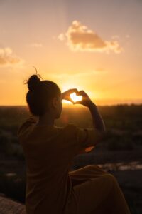 Girl making a heart with her hands in front of the sun